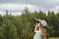 Young blonde woman bird watcher in cap and blue t-shirt looking through binoculars at cloudy sky in summer forest ornithological Royalty Free Stock Photo