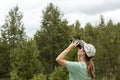 Young blonde woman bird watcher in cap and blue t-shirt looking through binoculars at cloudy sky in summer forest ornithological Royalty Free Stock Photo
