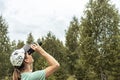 Young blonde woman bird watcher in cap and blue t-shirt looking through binoculars at cloudy sky in summer forest ornithological Royalty Free Stock Photo