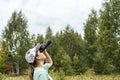 Young blonde woman bird watcher in cap and blue t-shirt looking through binoculars at cloudy sky in summer forest ornithological Royalty Free Stock Photo