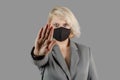 Young blonde woman in a black medical antiviral mask looks at the camera. Hand put forward, stop coronavirus