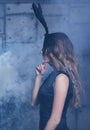 Young blonde woman in black rabbit or hare fancy mask and black dress. Female on smoke and metal wall background Royalty Free Stock Photo