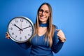 Young blonde woman with blue eyes holding big minute clock over isolated background with surprise face pointing finger to himself Royalty Free Stock Photo