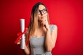 Young blonde woman with blue eyes wearing glasses holding graduated degree diploma serious face thinking about question, very Royalty Free Stock Photo