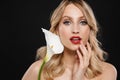 Young blonde woman with bright makeup red lips posing isolated over black wall background holding white flower Royalty Free Stock Photo