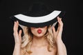 Young blonde woman with bright makeup red lips posing isolated over black wall background wearing hat blowing kisses Royalty Free Stock Photo