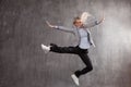 Young blonde woman in business suit and sneakers jumping for joy, gray textured background. Royalty Free Stock Photo