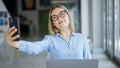 Young blonde woman business worker using laptop making selfie by smartphone at office Royalty Free Stock Photo