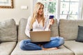 Young blonde woman buying using laptop and credit card sitting on the sofa at home Royalty Free Stock Photo
