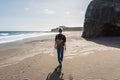 Young blonde woman with casual clothes and leather backpack walking on deserted windy beach