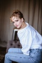 Young blonde woman in a casual white shirt and jeans in a loft interior, close up fashion portrait