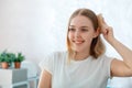 Young blonde woman combing her tangle hair with wooden comb hairbrush. Smiling beautiful woman, teenage girl do self Royalty Free Stock Photo