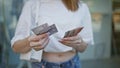 Young blonde woman counting swedish krone banknotes at street