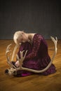 Young blonde woman crouching among caribou antlers in the studio