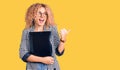 Young blonde woman with curly hair holding business folder pointing thumb up to the side smiling happy with open mouth Royalty Free Stock Photo