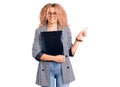 Young blonde woman with curly hair holding business folder smiling happy pointing with hand and finger to the side Royalty Free Stock Photo