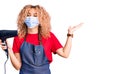 Young blonde woman with curly hair holding dryer blow wearing safety mask for coranvirus celebrating victory with happy smile and