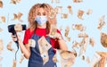 Young blonde woman with curly hair holding dryer blow wearing safety mask for coranvirus pointing finger to one self smiling happy