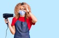 Young blonde woman with curly hair holding dryer blow wearing safety mask for coranvirus smiling happy doing ok sign with hand on