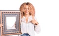 Young blonde woman with curly hair holding empty frame pointing finger to one self smiling happy and proud Royalty Free Stock Photo
