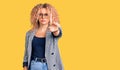Young blonde woman with curly hair wearing business jacket and glasses pointing with finger up and angry expression, showing no Royalty Free Stock Photo