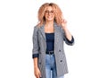 Young blonde woman with curly hair wearing business jacket and glasses showing and pointing up with finger number one while Royalty Free Stock Photo