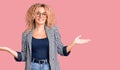 Young blonde woman with curly hair wearing business jacket and glasses smiling showing both hands open palms, presenting and Royalty Free Stock Photo