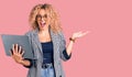 Young blonde woman with curly hair working using laptop screaming proud, celebrating victory and success very excited with raised Royalty Free Stock Photo
