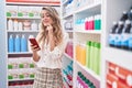 Young blonde woman customer smiling confident using smartphone at pharmacy