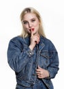 Young blonde woman in denim jaket and jeans shows Index finger to the lips on white background Royalty Free Stock Photo