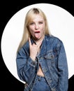 Young blonde woman in denim jaket and jeans shows tongue between two fingers on white background. indecent lifestyle Royalty Free Stock Photo