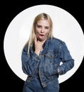 Young blonde woman in denim jaket and jeans shows tongue between two fingers on white background. indecent lifestyle Royalty Free Stock Photo