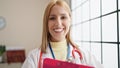 Young blonde woman doctor smiling confident holding clipboard at clinic Royalty Free Stock Photo