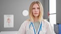 Young blonde woman doctor standing with serious expression at clinic