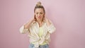 Young blonde woman doing derision expression with hands on ears over isolated pink background