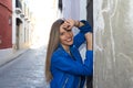 Young blonde woman dressed in blue leather jacket and jeans leaning against an old wall. The woman is happy and smiling with Royalty Free Stock Photo
