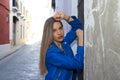 Young blonde woman dressed in blue leather jacket and jeans leaning against an old wall. The woman is sad and depressed and Royalty Free Stock Photo