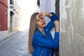 Young blonde woman dressed in blue leather jacket and jeans leaning against an old wall. The woman is sad and depressed and Royalty Free Stock Photo