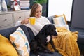 Young blonde woman drinking coffee sitting on sofa with dog at home Royalty Free Stock Photo