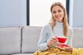 Young blonde woman drinking coffee sitting on sofa at home Royalty Free Stock Photo