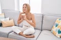 Young blonde woman drinking coffee sitting on sofa at home Royalty Free Stock Photo