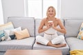 Young blonde woman drinking coffee sitting on sofa at home Royalty Free Stock Photo