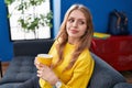 Young blonde woman drinking coffee sitting on sofa at street Royalty Free Stock Photo