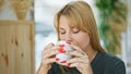 Young blonde woman drinking coffee sitting on table at coffee shop Royalty Free Stock Photo