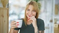 Young blonde woman drinking coffee sitting on table at coffee shop Royalty Free Stock Photo