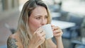 Young blonde woman drinking coffee sitting on table at coffee shop terrace Royalty Free Stock Photo