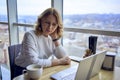 young blonde woman drinking coffee and working on a laptop in a cafe with panoramic windows and a view of the city from above Royalty Free Stock Photo