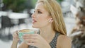 Young blonde woman drinking cup of coffee listening to music at coffee shop terrace Royalty Free Stock Photo