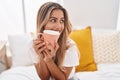 Young blonde woman drinking cup of coffee sitting on bed at bedroom Royalty Free Stock Photo