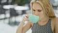Young blonde woman drinking cup of coffee sitting on table at coffee shop terrace Royalty Free Stock Photo
